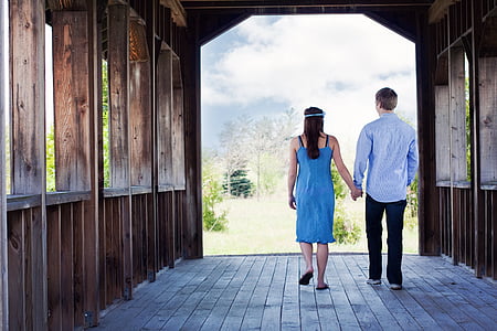 man and woman walking while holding hands near field of trees thumbnail