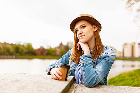 Woman Wearing Blue Denim Jacket Holding Coffee Cup Standing Near Concrete Platform thumbnail
