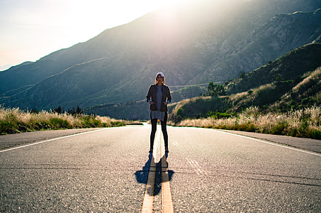 woman standing on asphalt road near mountains during daytime thumbnail