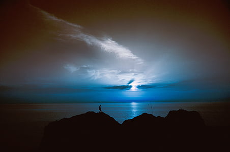 silhouette photo of person standing on rock formation near body of water thumbnail
