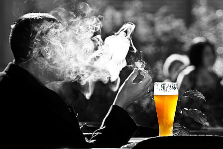 smoking man beside cup of beer selective color photography thumbnail