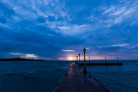 brown wooden dock with black lamps near sea during cloudy day thumbnail