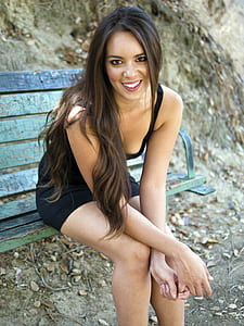 woman in black sleeveless mini dress sits on green wooden bench thumbnail