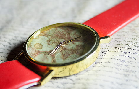 round beige analog watch with red strap on book thumbnail