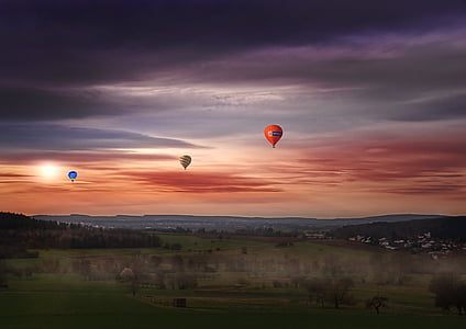 blue, yellow, and orange hot air balloons flying over green grass field during sunset thumbnail