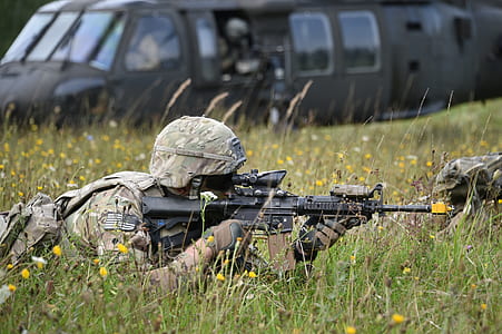 Army solider using black M4 with scope ducking on yellow petaled flowers field thumbnail