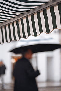 selective focus photography of man holding umbrella near black and white striped parasol during daytime thumbnail