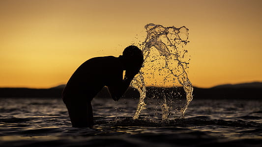 silhouette of person on rippling body of water against yellow sunlight thumbnail