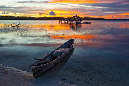 gray canoe on body of water near hut thumbnail