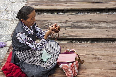 woman holding prayer beads while sitting on brown wooden board thumbnail