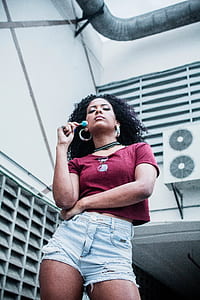 woman wearing red scoop-neck t-shirt and distressed blue denim short shorts holding blue lollipop thumbnail