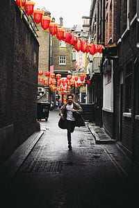 man running between concrete alley under lanterns at daytime thumbnail