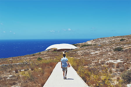 person in blue shirt walking on concrete pathway during day thumbnail