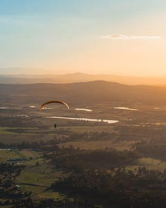 aerial photography of man on parachute floating above green field thumbnail