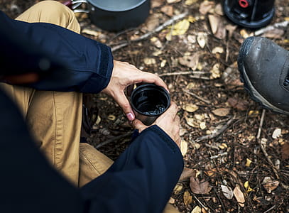 Person Holding Black and Gray Travel Mug With Sitting on Ground thumbnail