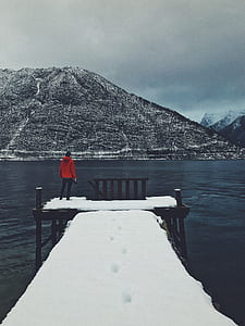person standing on snow coated wooden dock at cloudy sky thumbnail