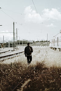 man in black backpack walking on grass near train thumbnail