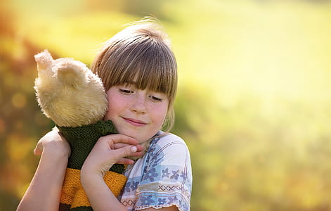 selective focus photography of girl hugging bear plush toy thumbnail