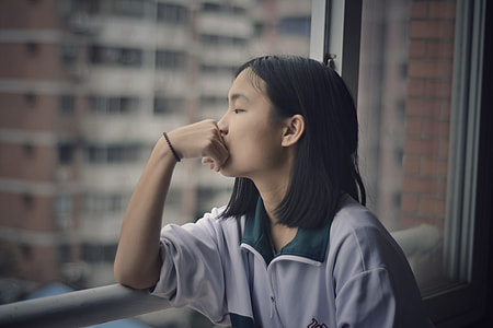 girl leaning against white metal railing looking out the window thumbnail