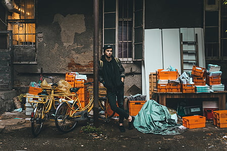 man in black hoodie, pants, and pair of shoes, leaning beside gray pole thumbnail