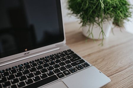 Silver Acer laptop on a wooden desk with a green plant, pencils and an Apple iPhone thumbnail