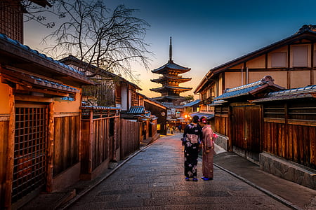 two person standing on gray concrete pavement near brown wooden houses thumbnail