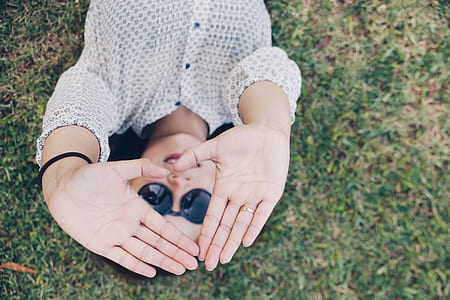 woman lying on green grass wearing sunglasses showing heart hand symbol thumbnail