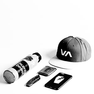 black-and-white VA 6-panel cap beside folding knife, smartphone, and bottle thumbnail
