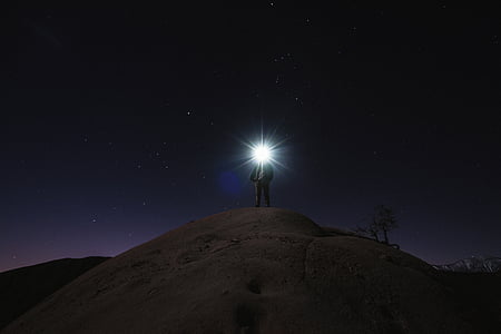 person on hill with white bright light at night time thumbnail