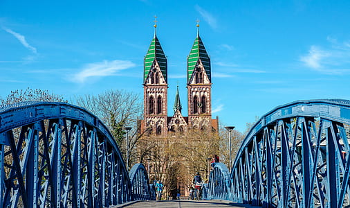 suspension bridge across brown and green cathedral under white and blue cloudy skies thumbnail