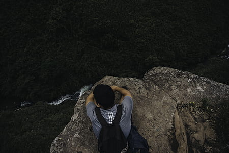 high angle photo of man lying on mountain cliff watching body of water thumbnail