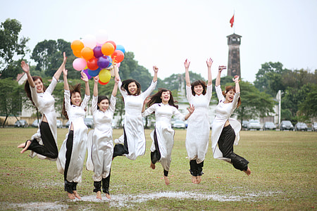 jump shot photo seven women wearing white dress and black pants in grass field thumbnail
