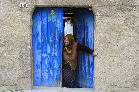 woman in brown top coming out from blue wooden door thumbnail