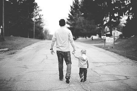 grayscale photo of man and children walking on road thumbnail