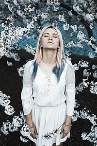 woman with blond hair and blue tip highlights with closed eyes in the middle of white flowers thumbnail