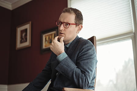 man holding chin while sitting near glass window during daytime thumbnail