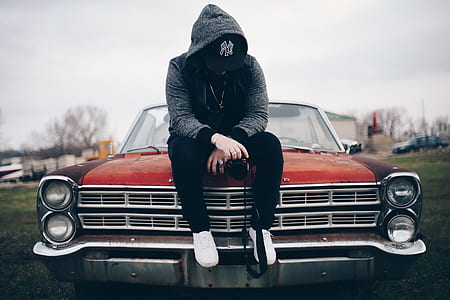 person in gray hoodie jacket sitting on red car thumbnail