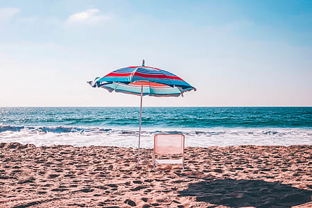 white lounge under multicolored parasol on seashore at daytime thumbnail