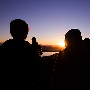 silhouette photography of two children facing body of water and mountain under clear blue sky thumbnail