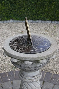 grey and brown sun dial near green leafed plants thumbnail