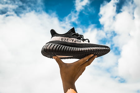 person holding black and white adidas Yeezy Boost 350 V2 shoe under blue sky thumbnail