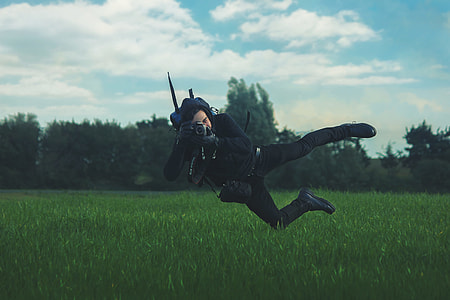 man jumps while pointing black camera on green grass thumbnail