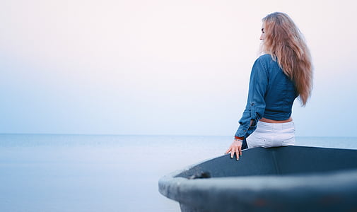 woman wears blue long-sleeved shirt sits on black rowboat under cloudy sky during daytime thumbnail