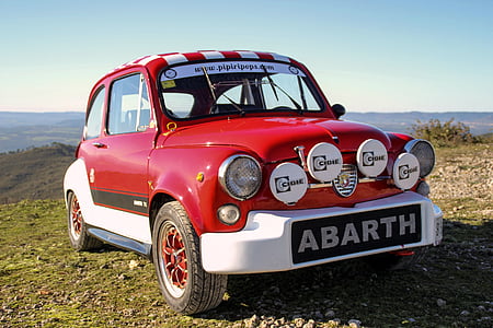 classic red and white Abarth coupe parked on ground under blue sky thumbnail