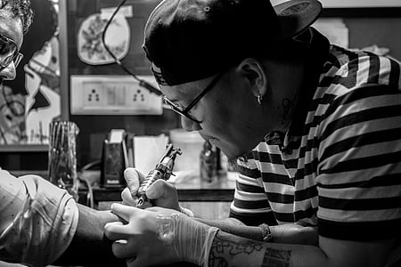 grayscale photo of man doing tattoo thumbnail
