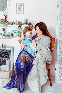 Woman in Blue White and Brown Dress Holding Baby in Teal Dress Inside House thumbnail