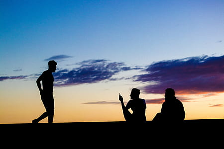 silhouette of two men sitting and looking at man walking under clear day sky thumbnail