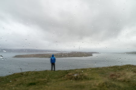 man standing on green grass near body of water during rainy day thumbnail