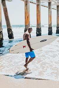 man walking on shore carrying surfboard during day thumbnail
