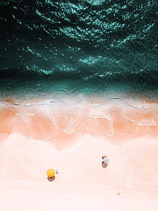 aerial view photography of two yellow and white umbrellas on seashore near ocean thumbnail